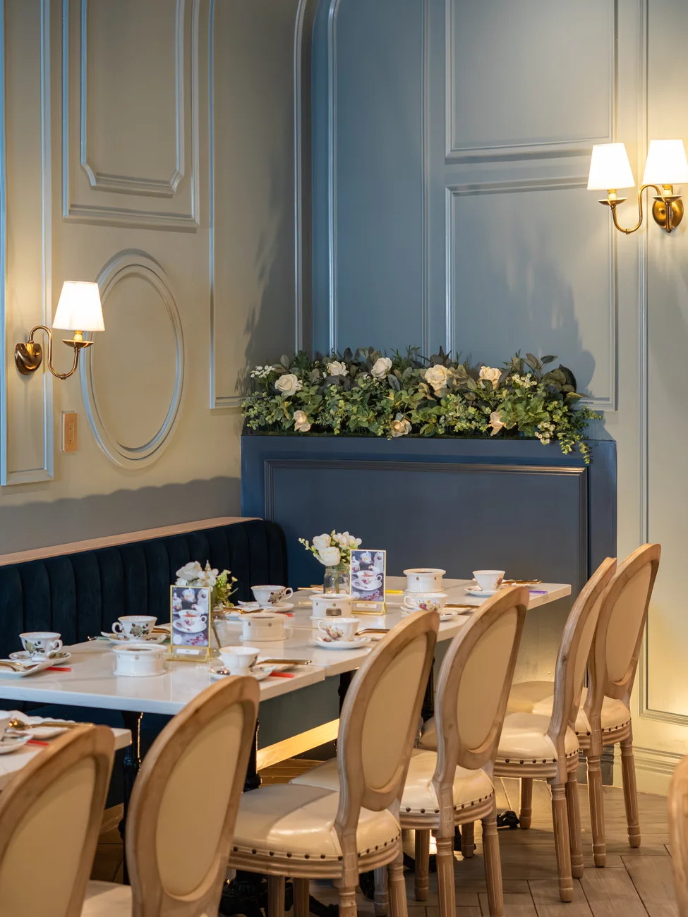 Blue paneled dining room with upholstered seating and tables set for tea